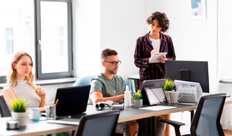 Personas trabajando en una oficina moderna con computadoras y plantas
