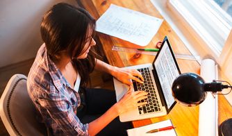 Mujer escribiendo en laptop sobre un escritorio con planos y lámpara