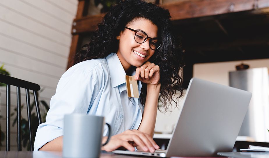 Mujer sonriendo mientras paga con tarjeta frente a su portátil