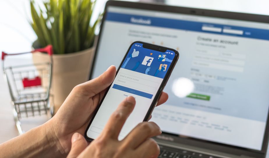 Usuario iniciando sesión en Facebook desde su celular frente a laptop