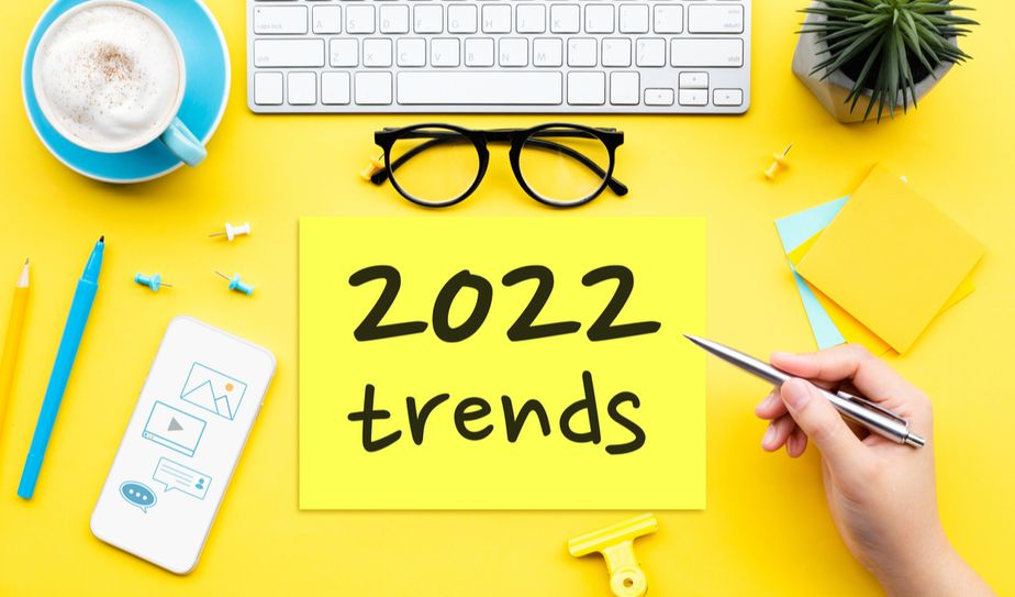 Mesa amarilla con taza de café, gafas y cartel que dice 2022 trends
